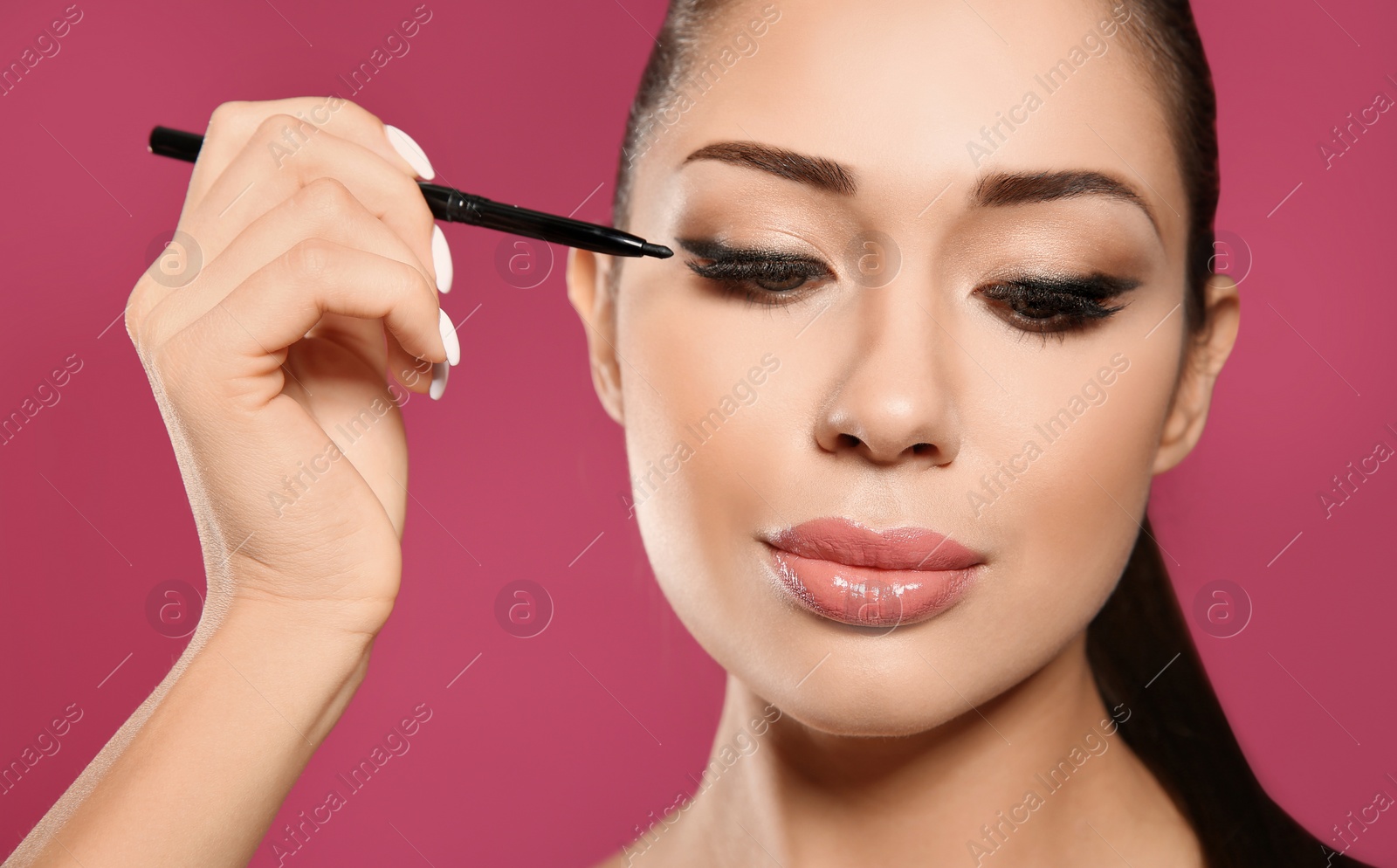 Photo of Beautiful woman applying eyeliner on pink background, closeup. Stylish makeup