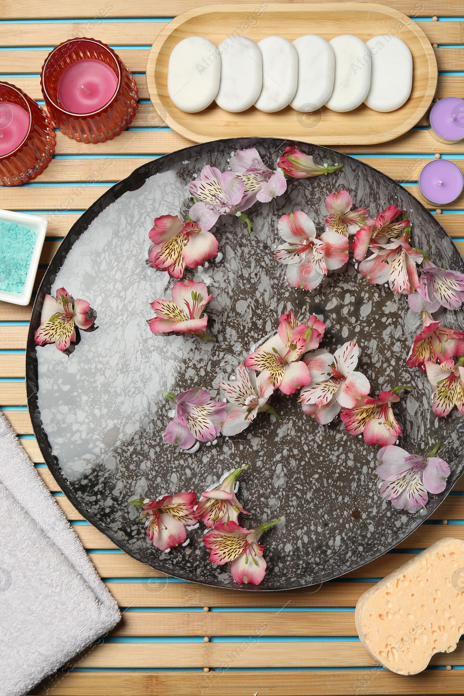 Photo of Bowl of water with flowers and different spa supplies on wooden mat, flat lay