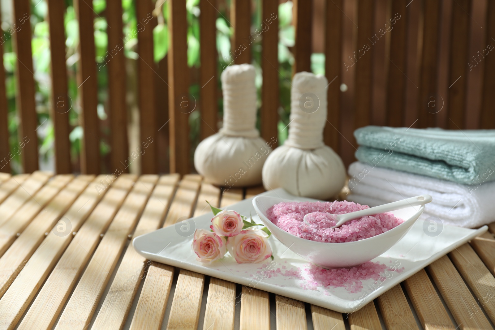 Photo of Bowl of pink sea salt and beautiful roses on wooden table, space for text