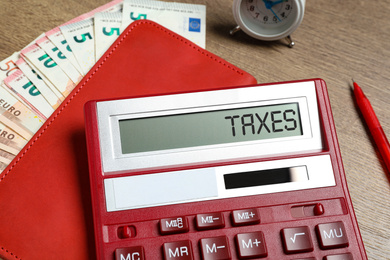 Image of Calculator with word Taxes, notebook and money on table, closeup