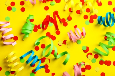Photo of Colorful serpentine streamers and confetti on yellow background, flat lay