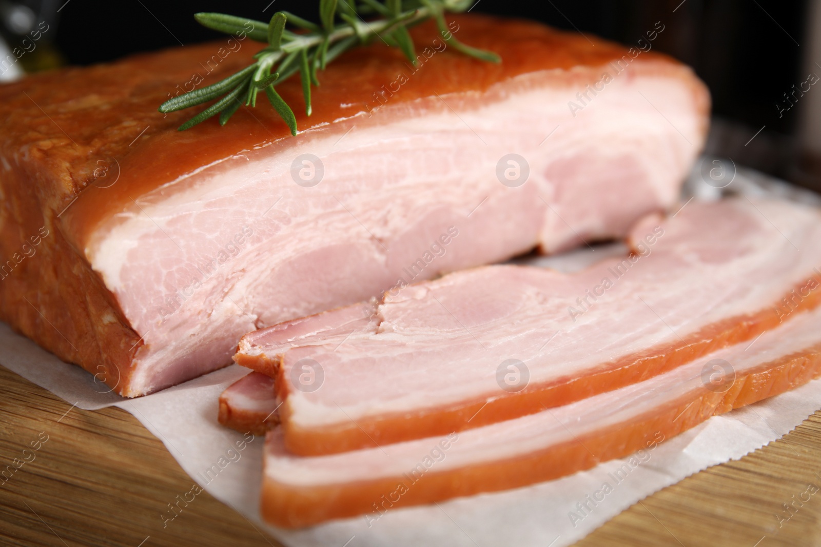 Photo of Delicious smoked bacon with rosemary on wooden board, closeup