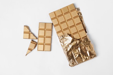 Photo of Shiny golden chocolate bar with foil on white background, top view
