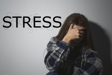 Image of Depressed young woman near white wall and word STRESS 