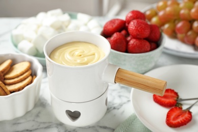 Photo of Fondue pot with white chocolate and different products on marble table