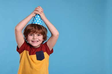 Photo of Birthday celebration. Cute little boy in party hat on light blue background, space for text