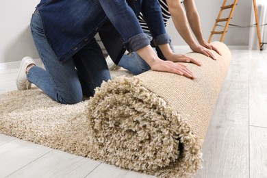 Photo of Couple unrolling new carpet in room, closeup