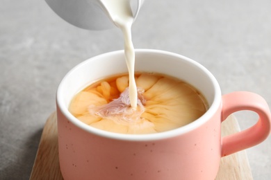 Photo of Pouring milk into cup of black tea on gray table, closeup