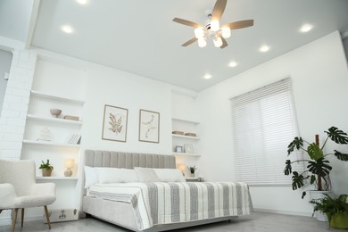 Comfortable furniture, ceiling fan, houseplants and accessories in stylish bedroom, low angle view