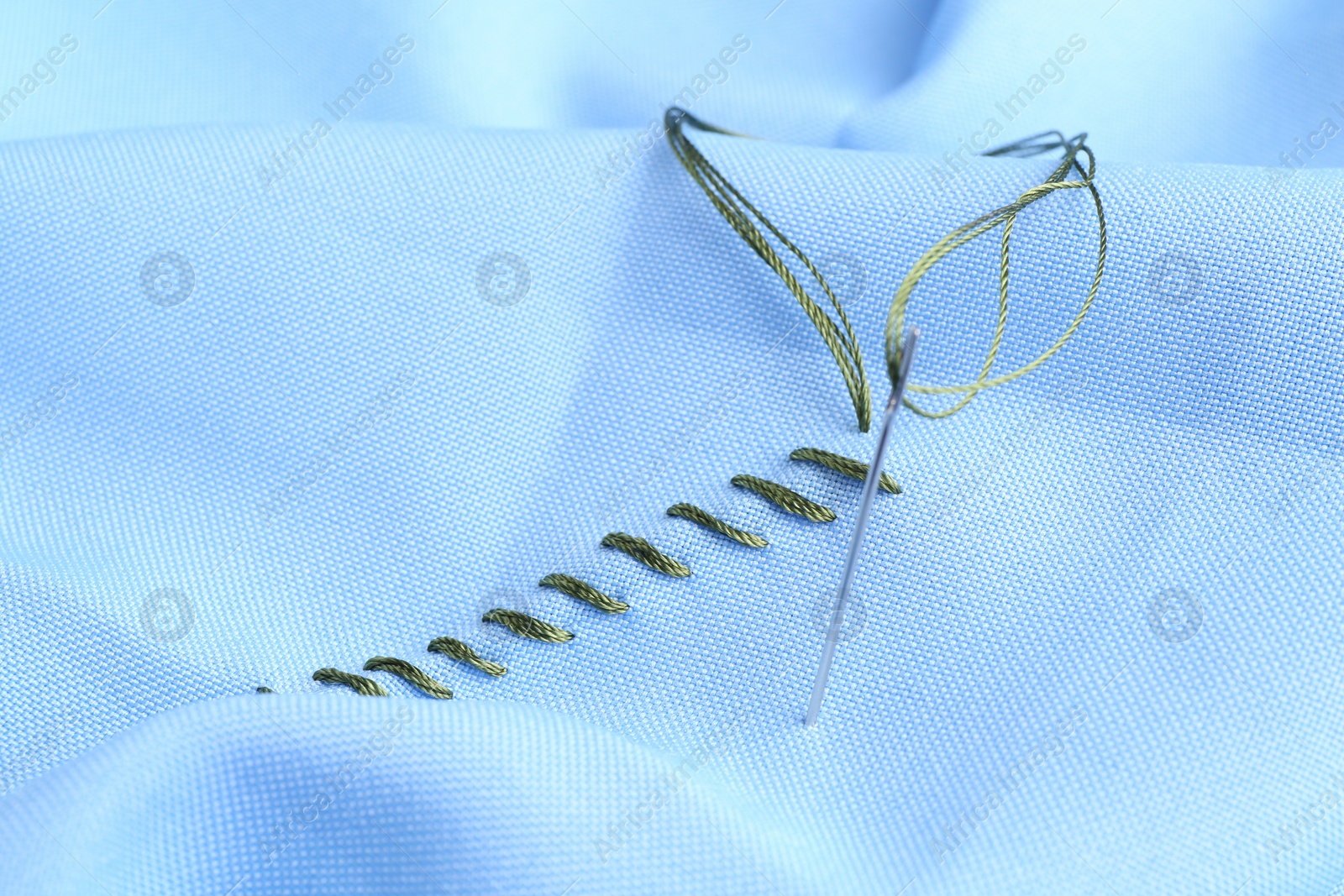 Photo of Sewing needle with thread and stitches on light blue cloth, closeup