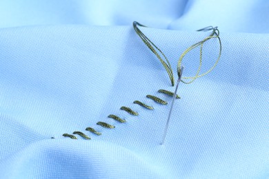 Sewing needle with thread and stitches on light blue cloth, closeup