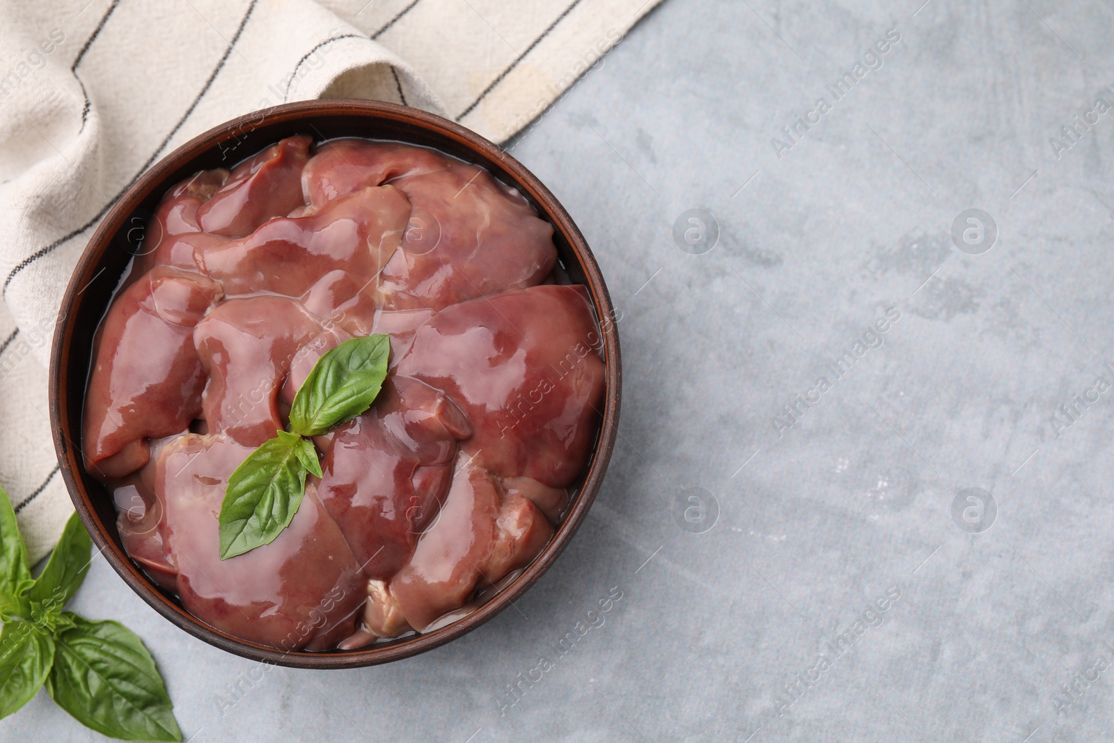 Photo of Bowl with raw chicken liver and basil on light grey table, flat lay. Space for text