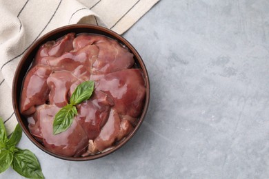 Bowl with raw chicken liver and basil on light grey table, flat lay. Space for text