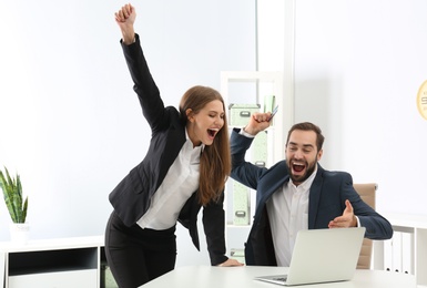 Photo of Emotional young people with credit card and laptop celebrating victory in office