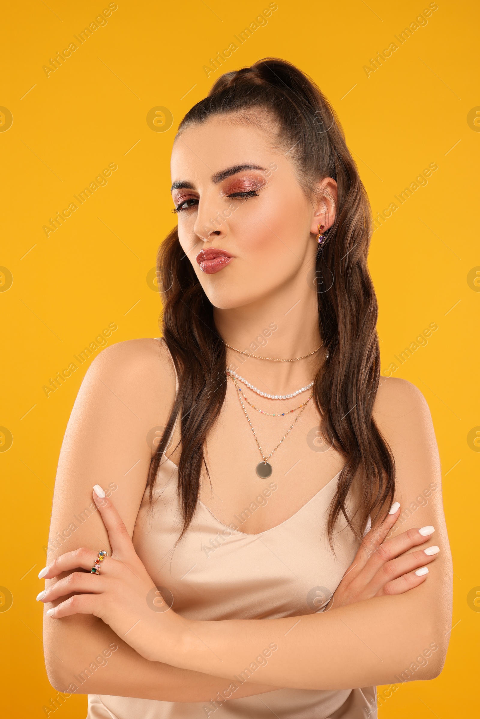 Photo of Beautiful woman with elegant jewelry blowing kiss on orange background