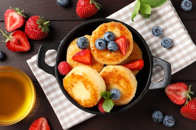 Delicious cottage cheese pancakes with fresh berries and honey on wooden table, flat lay
