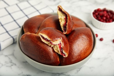 Delicious baked cranberry pirozhki in bowl on white marble table