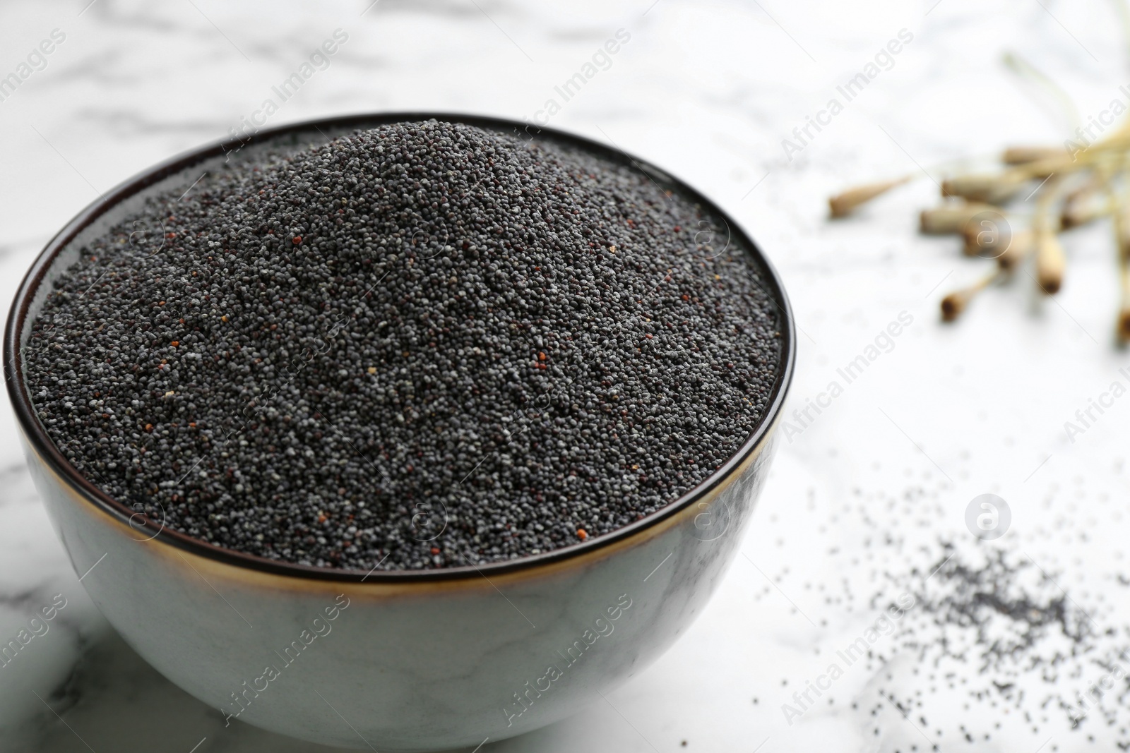 Photo of Poppy seeds in bowl on white marble table