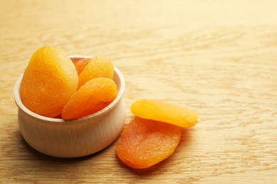 Photo of Bowl of tasty apricots on wooden table, space for text. Dried fruits