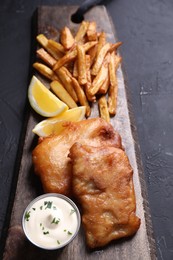 Tasty fish, chips, lemon and sauce on black table, closeup