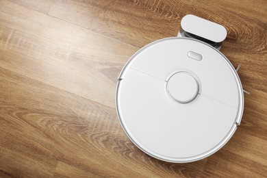 Robotic vacuum cleaner charging on wooden floor, top view. Space for text