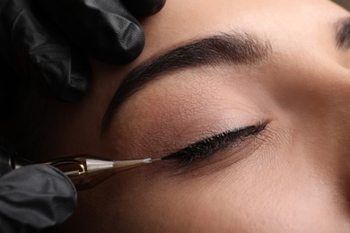 Photo of Young woman undergoing procedure of permanent eye makeup in tattoo salon, closeup
