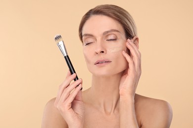 Woman with swatch of foundation holding makeup brush on beige background
