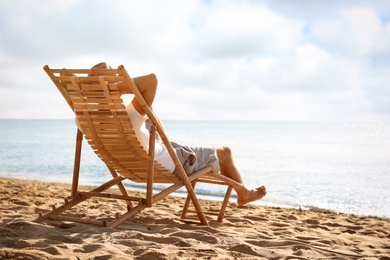 Photo of Man relaxing on deck chair at sandy beach. Summer vacation