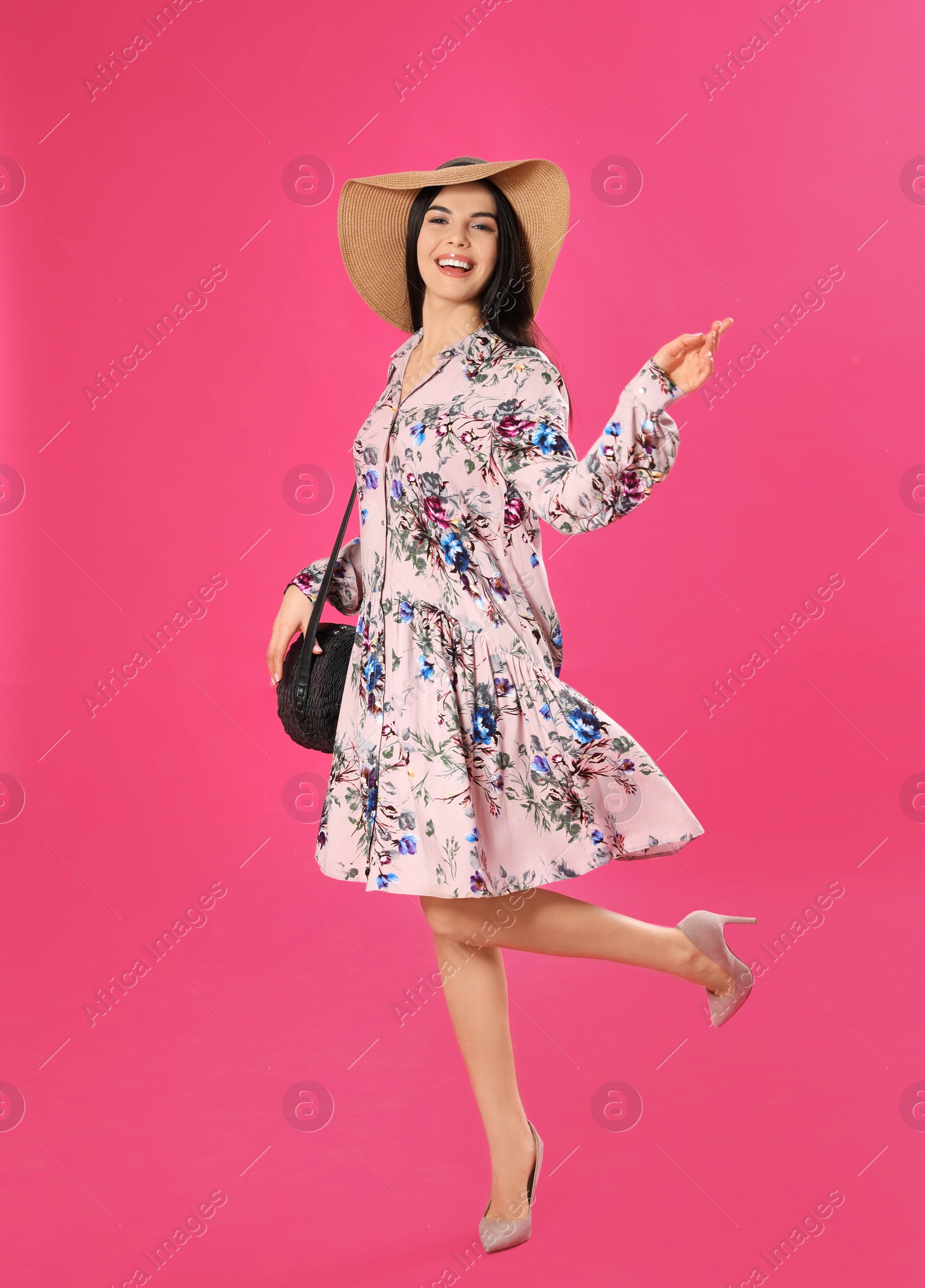Photo of Young woman wearing floral print dress and straw hat on pink background