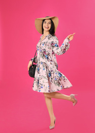 Young woman wearing floral print dress and straw hat on pink background