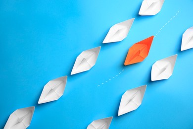 Orange paper boat floating between others on light blue background, flat lay. Uniqueness concept