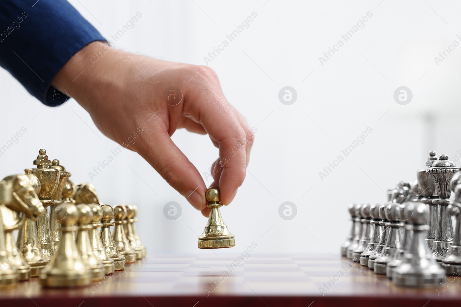 Photo of Man with game piece playing chess at checkerboard against white background, closeup