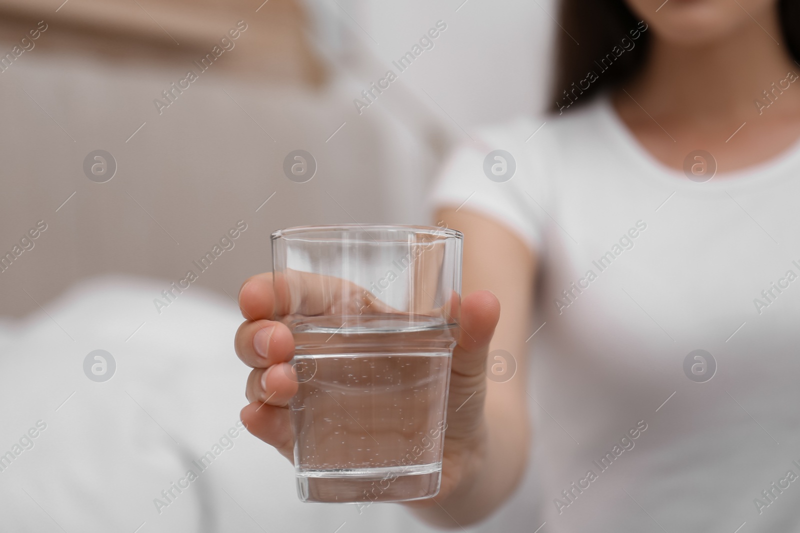 Photo of Woman holding glass of water in bedroom, closeup