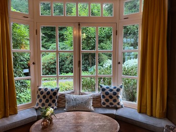 Photo of Wooden table near bay window seat with cushions in cozy room. Interior design