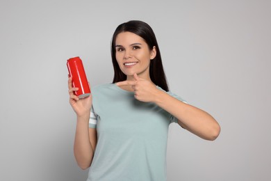 Beautiful young woman holding red tin can with beverage on light grey background