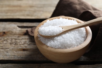 Organic salt in bowl and spoon on wooden table, closeup. Space for text