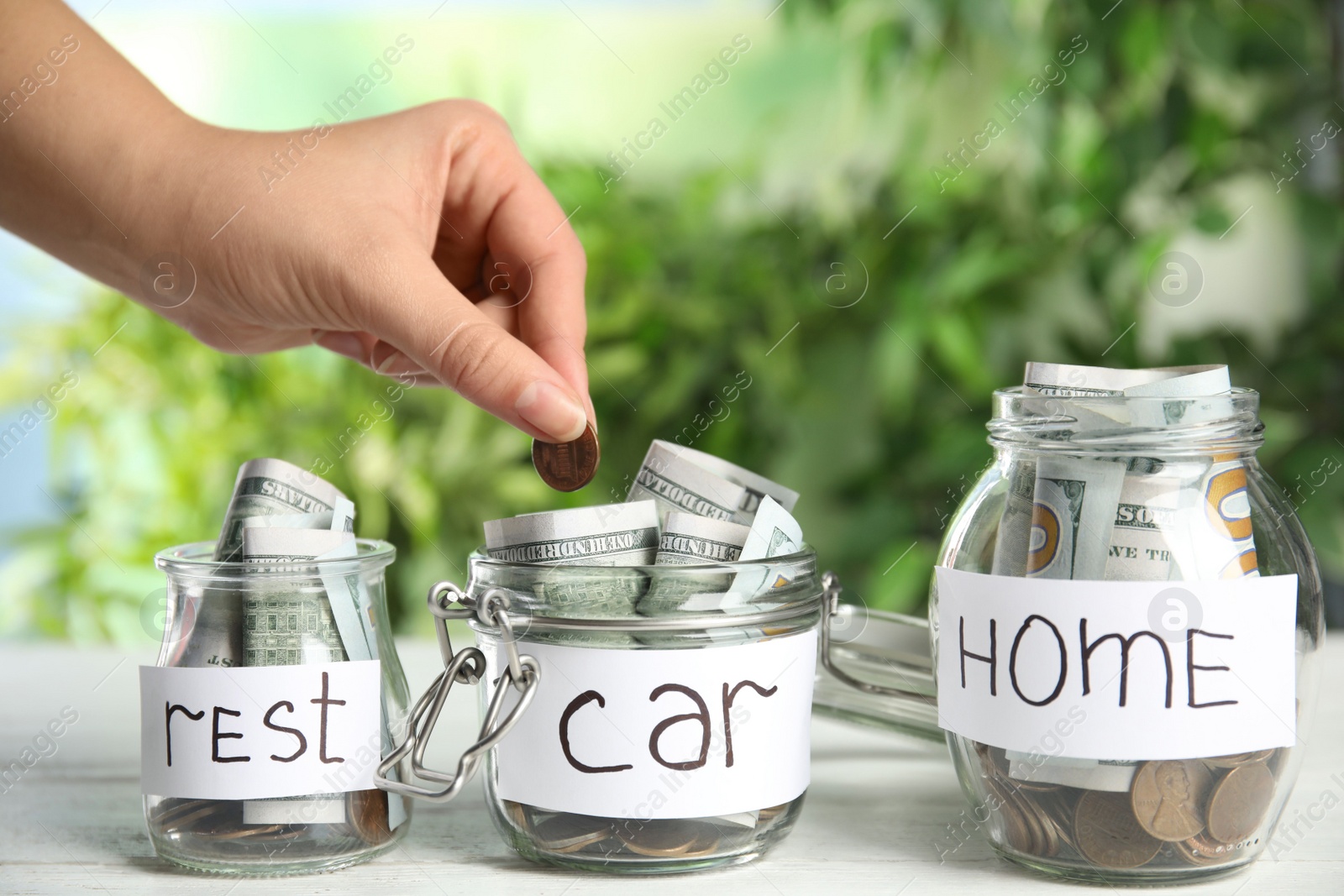 Photo of Woman putting coin into jar with tag CAR on white wooden table, closeup