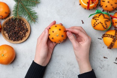 Woman decorating fresh tangerine with cloves at grey table, top view