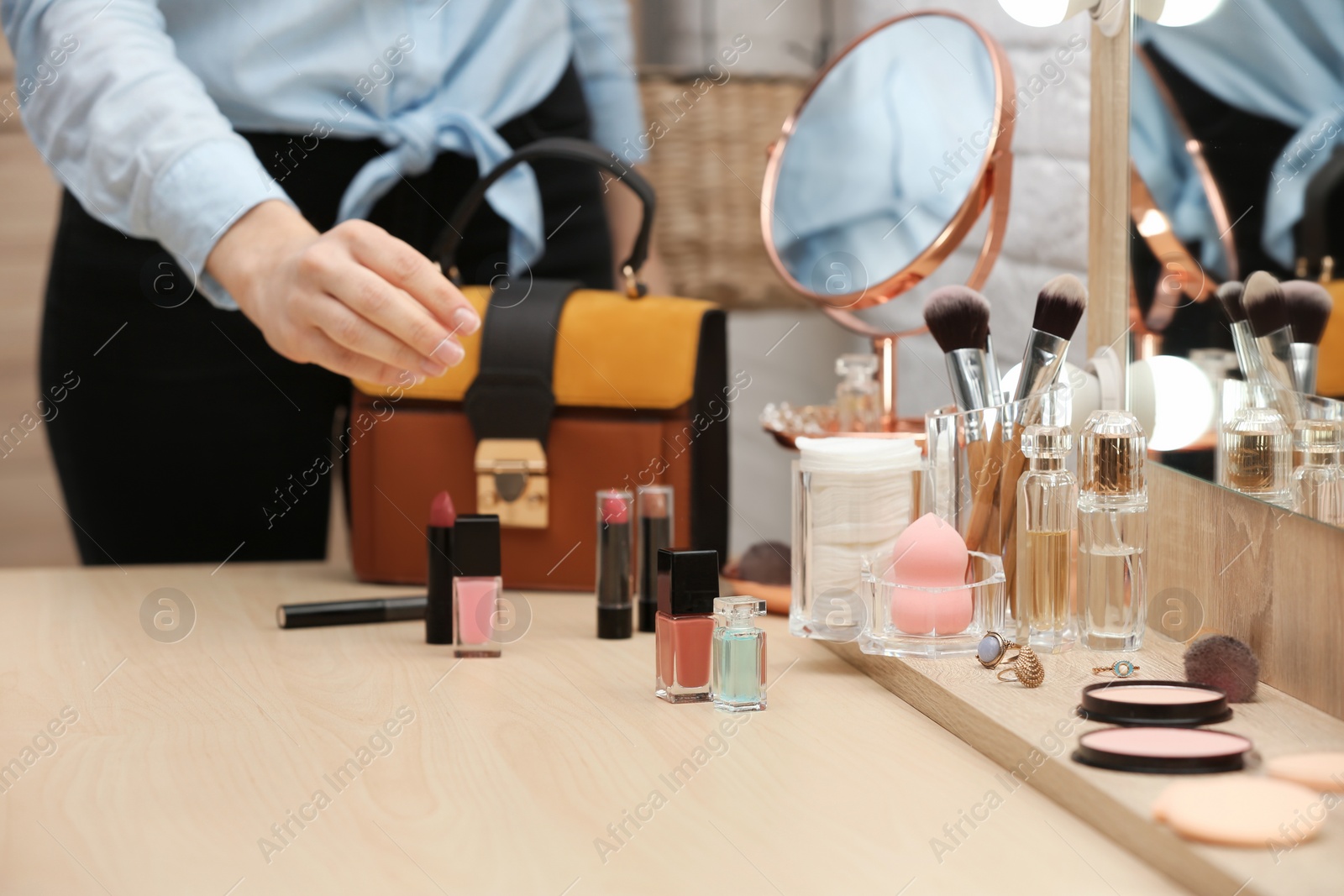 Photo of Woman reaching for cosmetic products on dressing table, closeup. Professional makeup