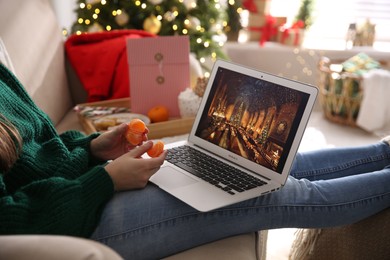Photo of MYKOLAIV, UKRAINE - DECEMBER 25, 2020: Woman with tangerine watching Harry Potter and Philosopher's stone movie on laptop at home, closeup. Cozy winter holidays atmosphere