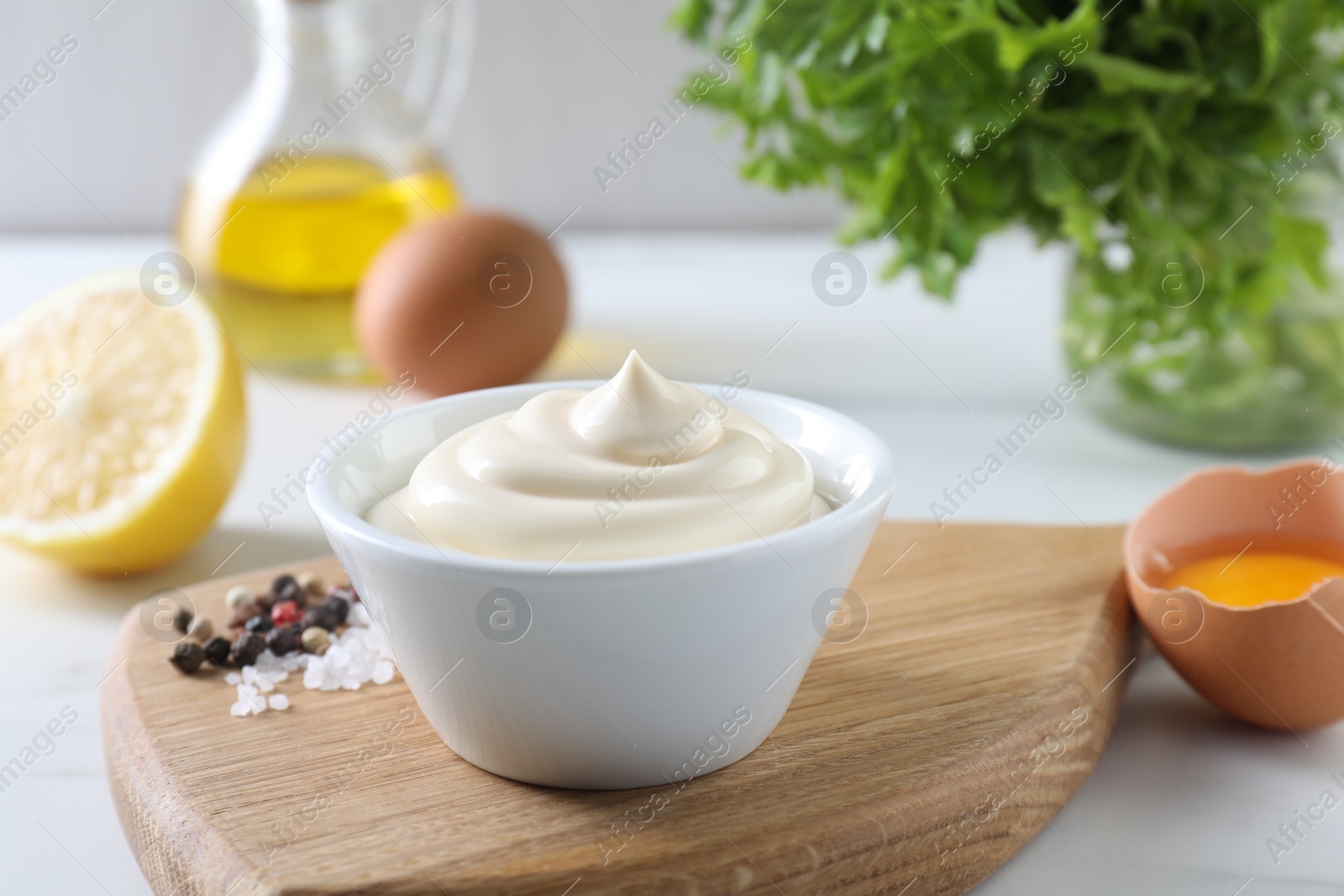 Photo of Tasty mayonnaise sauce in bowl, spices and ingredients on white table, closeup