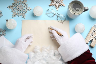 Photo of Top view of Santa writing letter at light blue table, closeup. Space for text