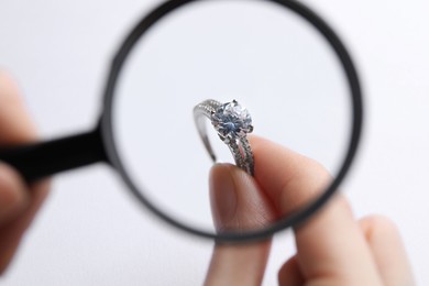 Photo of Jeweler examining diamond ring with magnifying glass at white background, closeup