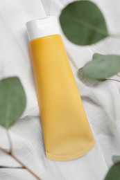 Photo of Tube of face cleansing product and eucalyptus leaves on white fabric, flat lay