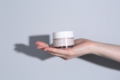 Photo of Woman holding jar of cream on grey background, closeup