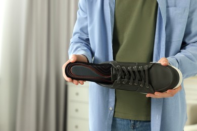 Man putting orthopedic insole into shoe indoors, closeup