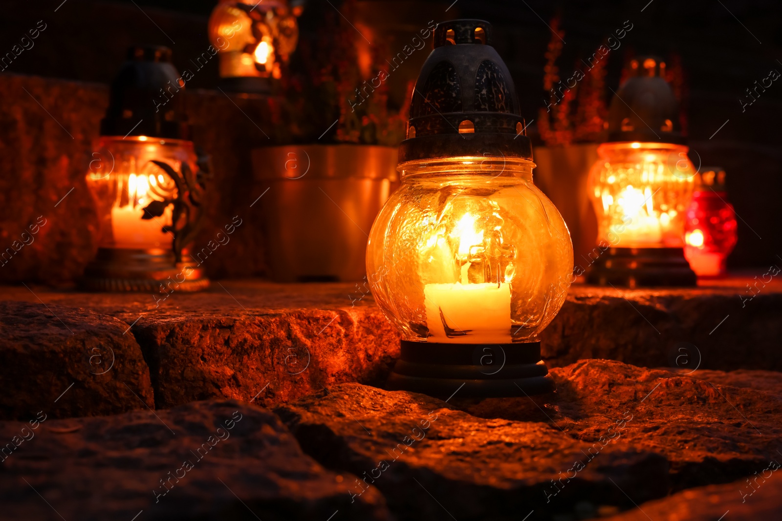 Photo of Different grave lanterns with burning candles on stone surface at night