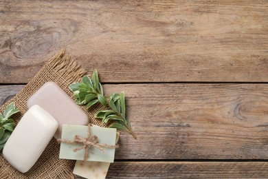 Soap bars and green plants on wooden table, flat lay. Space for text