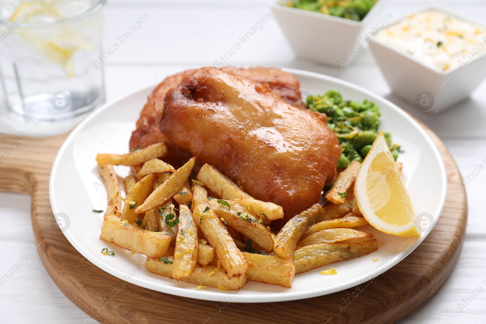 Photo of Tasty fish, chips, sauce, peas and lemon on white wooden table, closeup