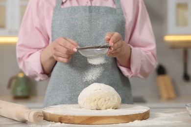 Making bread. Woman sifting flour onto dough at white table in kitchen, closeup